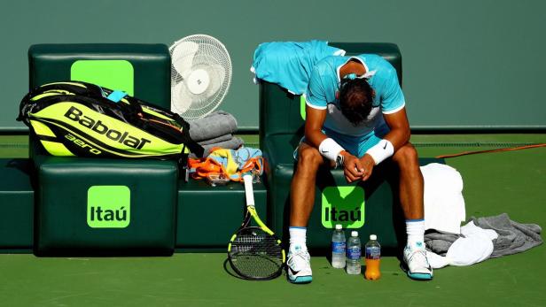 Ein Tennisspieler sitzt erschöpft auf einer Bank neben seiner Ausrüstung.
