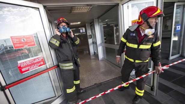 Zwei Feuerwehrleute stehen vor einem Eingang, einer setzt eine Gasmaske auf.