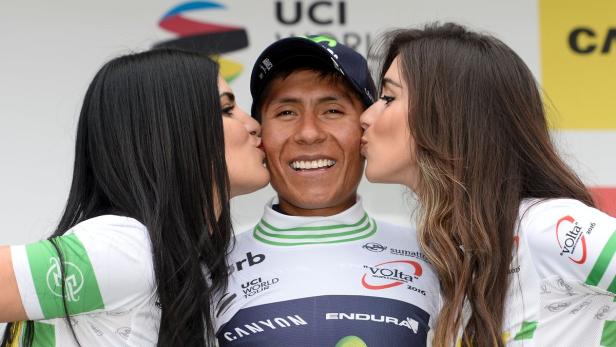 Ein Radrennfahrer wird von zwei Frauen auf dem Siegerpodest geküsst.