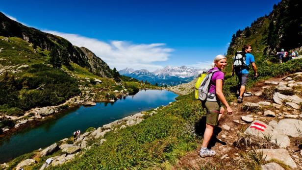 Wanderer genießen die Aussicht auf einen Bergsee und die schneebedeckten Gipfel im Hintergrund.