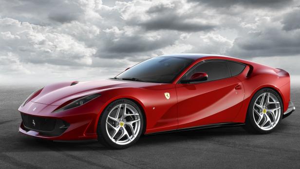 Ein roter Ferrari steht vor einem bewölkten Himmel.