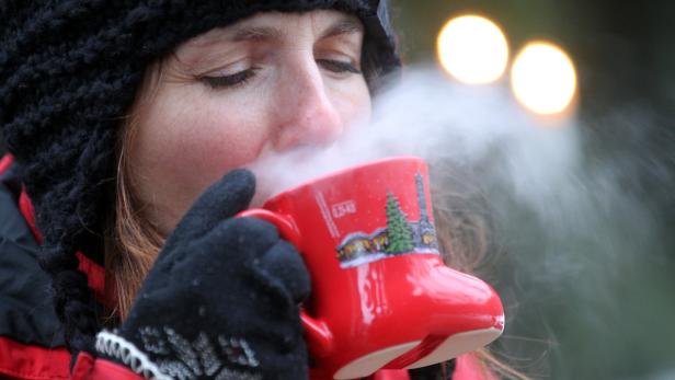 Eine Frau mit Mütze trinkt aus einer roten Tasse, aus der Dampf aufsteigt.