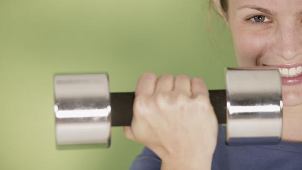 Eine Frau hält eine Hantel vor einem grünen Hintergrund.