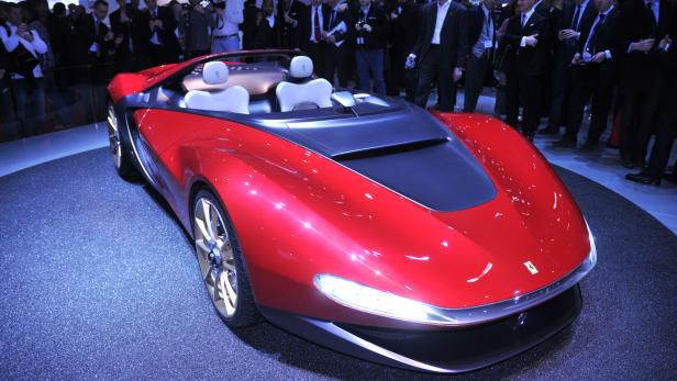 Ein roter Ferrari steht auf einer Bühne, umringt von Menschen.