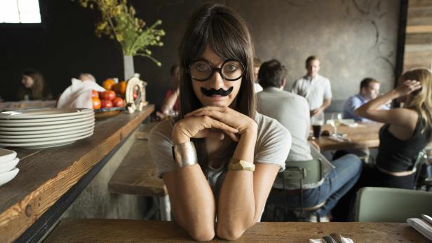 Eine Frau mit Brille und aufgeklebtem Schnurrbart sitzt in einem Restaurant.