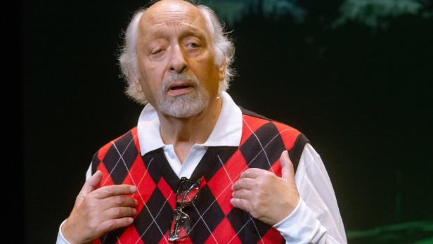 Ein älterer Mann mit grauem Haar und Bart trägt eine rot-schwarze Argyle-Weste.