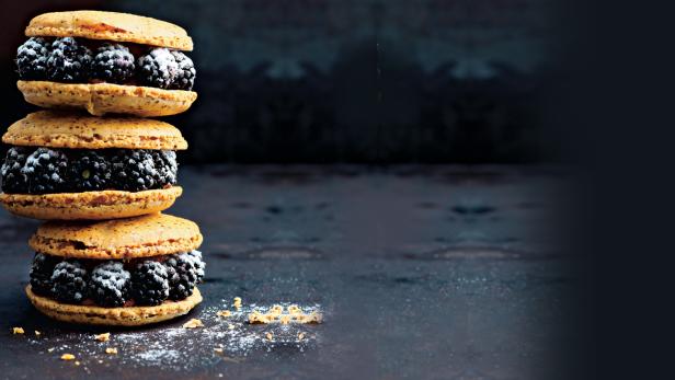 Ein Stapel von drei Brombeer-Macarons auf einem dunklen Untergrund.