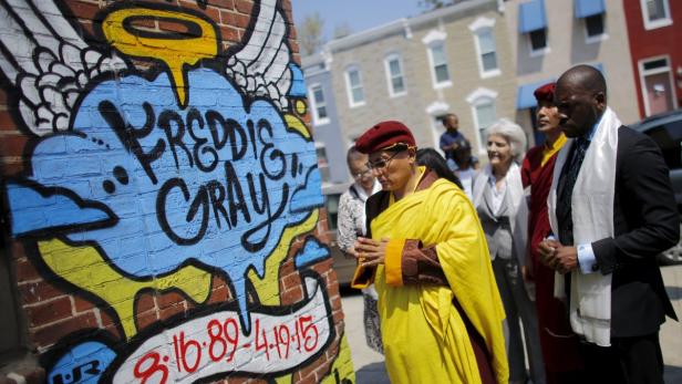 Eine Gruppe von Menschen steht vor einem Graffiti-Wandbild für Freddie Gray.