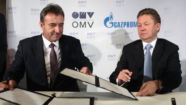 Zwei Männer in Anzügen unterzeichnen ein Abkommen vor den Logos von OMV und Gazprom.
