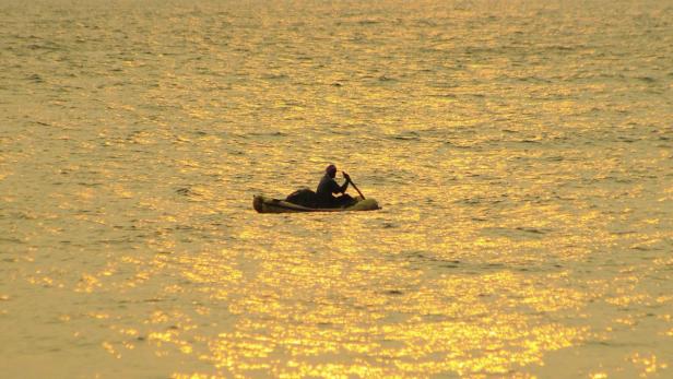 Eine Person paddelt bei Sonnenuntergang in einem kleinen Boot auf dem Wasser.