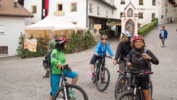 Eine Gruppe Radfahrer macht eine Pause auf einem Dorfplatz.