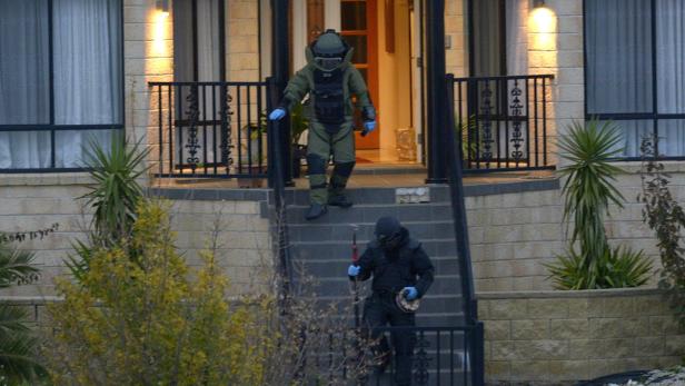 Zwei Entschärfer in Schutzanzügen steigen eine Treppe vor einem Haus hinunter.