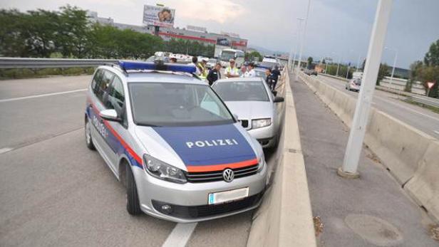 Ein Polizeiauto steht auf einer Autobahn neben einer Betonmauer.