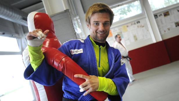 Ein lächelnder Judoka umarmt eine rote Trainingspuppe.