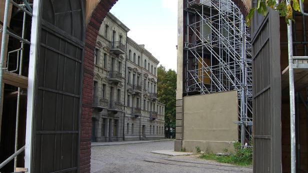 Ein Blick durch ein Tor auf eine Straße mit alten Gebäuden und Baugerüsten.
