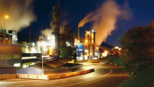 Eine Industrieanlage mit beleuchteten Türmen und aufsteigendem Rauch in der Nacht.