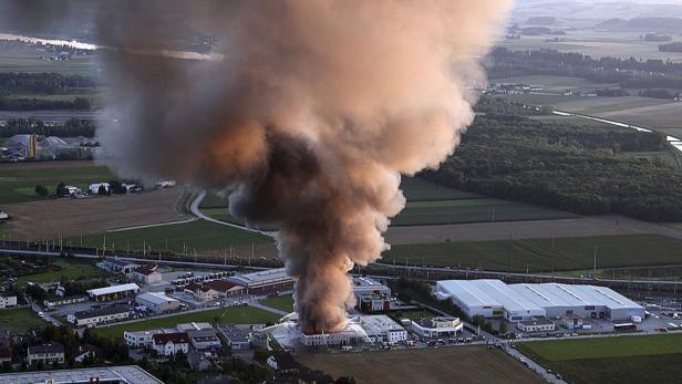 Ein großes Feuer in einem Industriegebiet mit dichter Rauchwolke über Feldern.