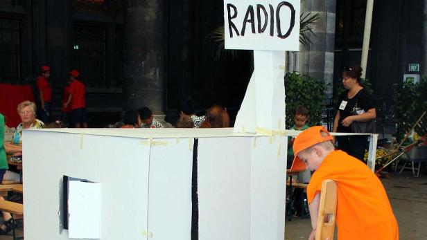 Ein Kind kehrt vor einem improvisierten Radiostudio aus Pappe.