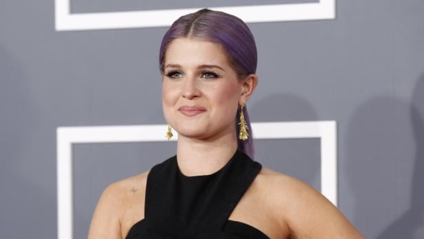 Kelly Osbourne mit lila Haaren und goldenen Ohrringen auf einem roten Teppich.