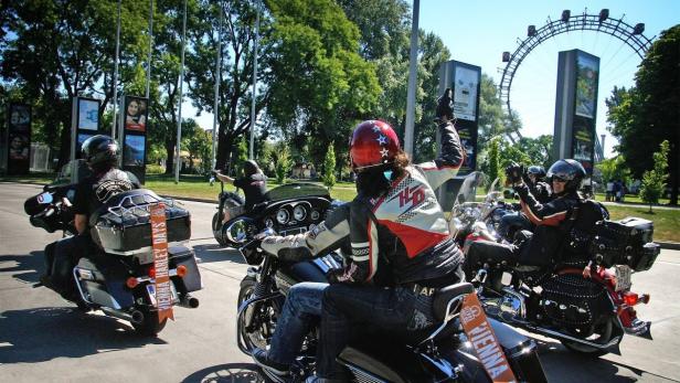 Eine Gruppe von Motorradfahrern fährt auf der Straße in Wien, im Hintergrund das Riesenrad.