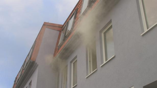 Rauch dringt aus einem Gebäude mit grauer Fassade.