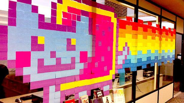 Ein Nyan Cat-Mosaik aus bunten Haftnotizen an einer Bürowand.