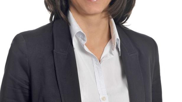 Eine Frau mit braunen Haaren und blauem Blazer lächelt in die Kamera.