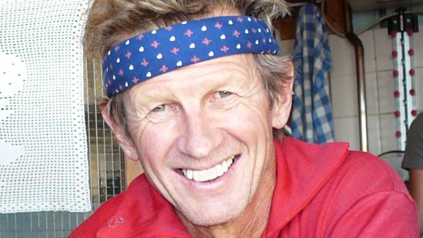 Ein lächelnder Mann mit Stirnband und rotem Hemd.