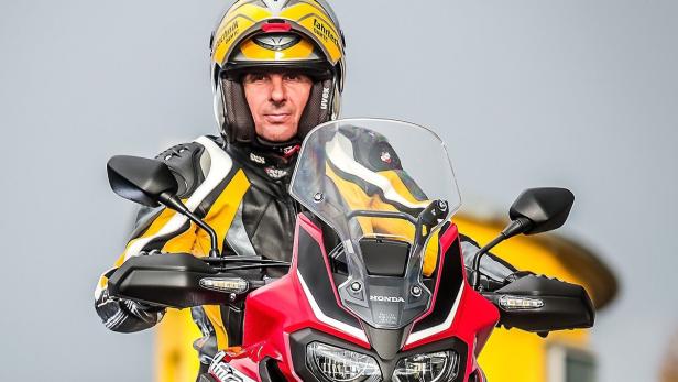 Ein Mann mit gelbem Helm sitzt auf einem roten Honda-Motorrad.