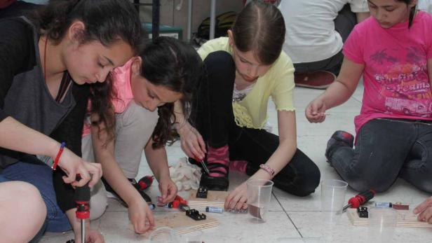Mehrere Mädchen sitzen auf dem Boden und arbeiten an kleinen elektronischen Projekten.