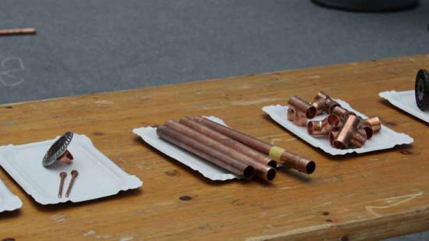 Kupferrohre, Verbinder, Nieten und Drahtspulen liegen auf einem Holztisch bereit.