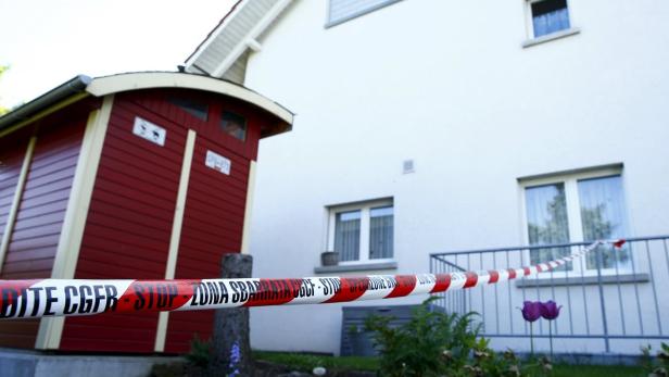 Ein rot-weißes Absperrband vor einem Haus und einem kleinen Schuppen.