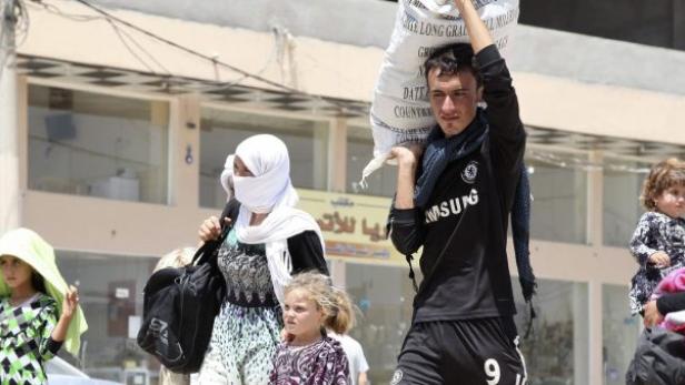 Eine Gruppe von Menschen, darunter Kinder, geht mit Habseligkeiten auf einer Straße entlang.