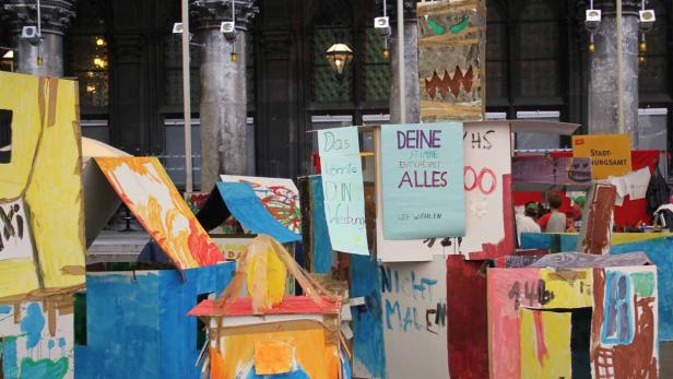 Eine Installation aus bemalten Papphäusern und Wahlplakaten in einem Innenraum.