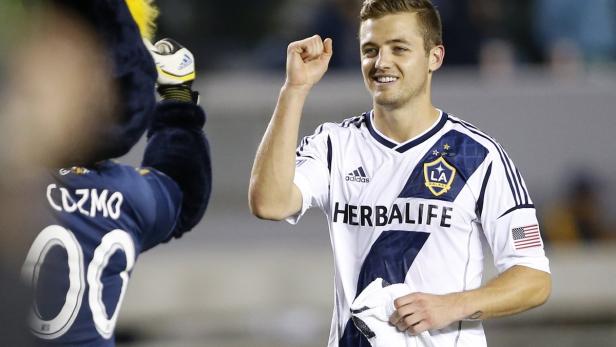 Ein lächelnder Fußballspieler von LA Galaxy jubelt neben dem Maskottchen Cozmo.