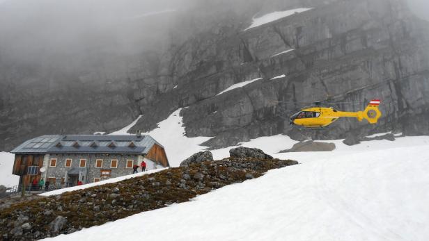 Ein gelber Hubschrauber fliegt in den Bergen in der Nähe eines Hauses.