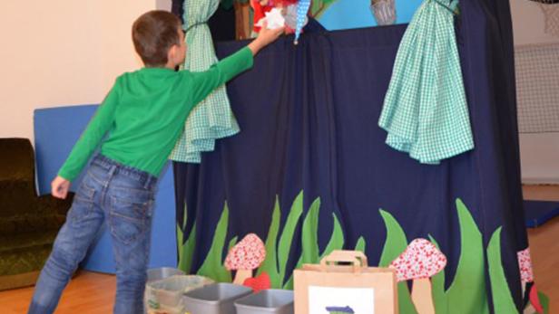 Ein Junge spielt mit einer Handpuppe vor einem dekorierten Vorhang.