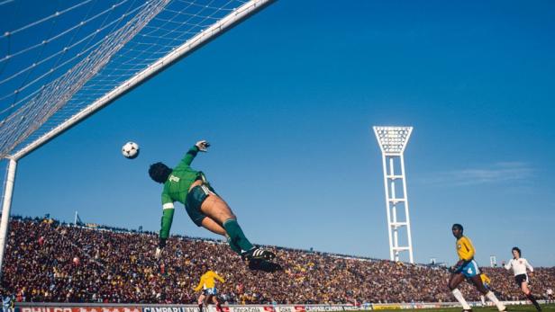 Ein Torwart springt, um einen Fußball vor einem vollen Stadion zu fangen.
