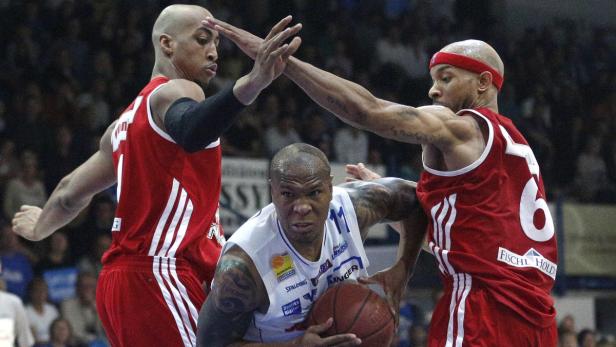 Drei Basketballspieler kämpfen um den Ball während eines Spiels.
