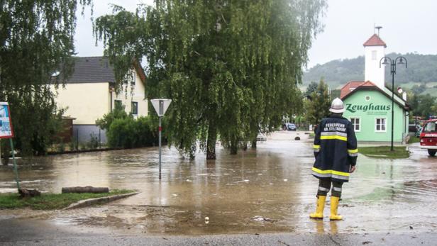 Ein Feuerwehrmann steht vor einem überfluteten Dorf.
