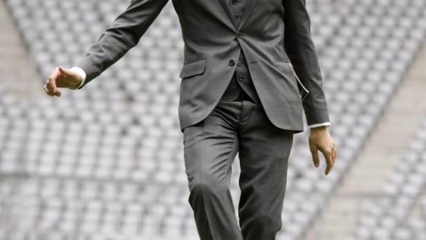 Pep Guardiola im Anzug spielt mit einem Fußball auf dem Rasen.