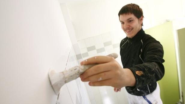 Ein junger Mann streicht eine Wand mit einem Pinsel weiß.