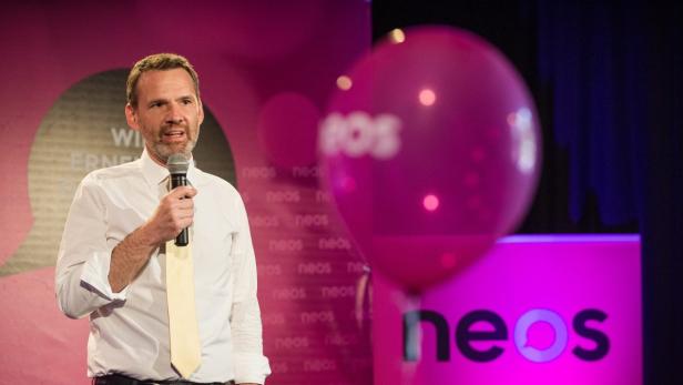 Ein Mann mit Mikrofon spricht vor einem Hintergrund mit dem Logo der Partei NEOS.