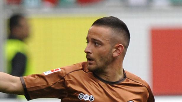 Ein Fußballspieler in braunem Trikot blickt aufmerksam zur Seite.