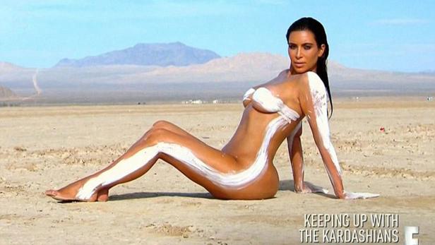 Kim Kardashian posiert mit weißer Farbe bemalt in einer Wüstenlandschaft.