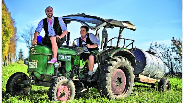 Zwei Männer in Tracht sitzen auf einem grünen Traktor mit der Aufschrift „Polizei“.