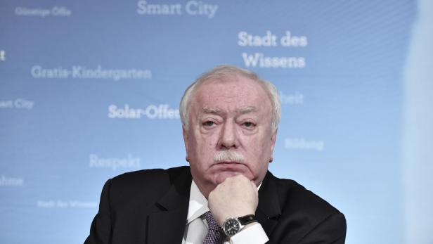 Ein Mann mit Schnurrbart posiert vor einer Wand mit den Worten „Smart City“ und „Gratis-Kindergarten“.