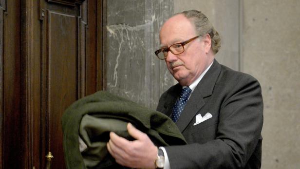 Ein Mann mit Brille und Anzug hält eine grüne Jacke in den Händen.