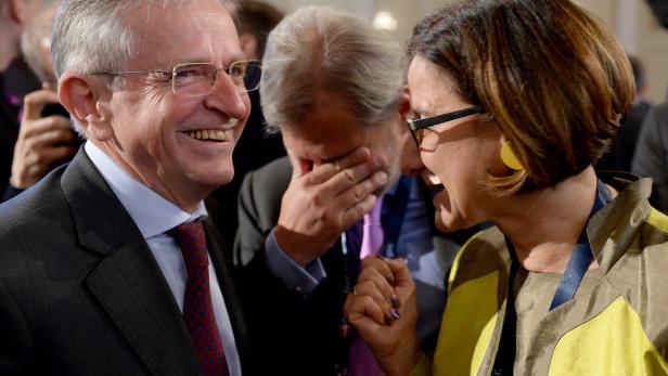 Ein lachender Mann im Anzug unterhält sich mit einer Frau mit gelber Jacke.