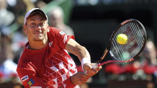 Ein Tennisspieler in rotem Hemd schlägt einen gelben Tennisball.
